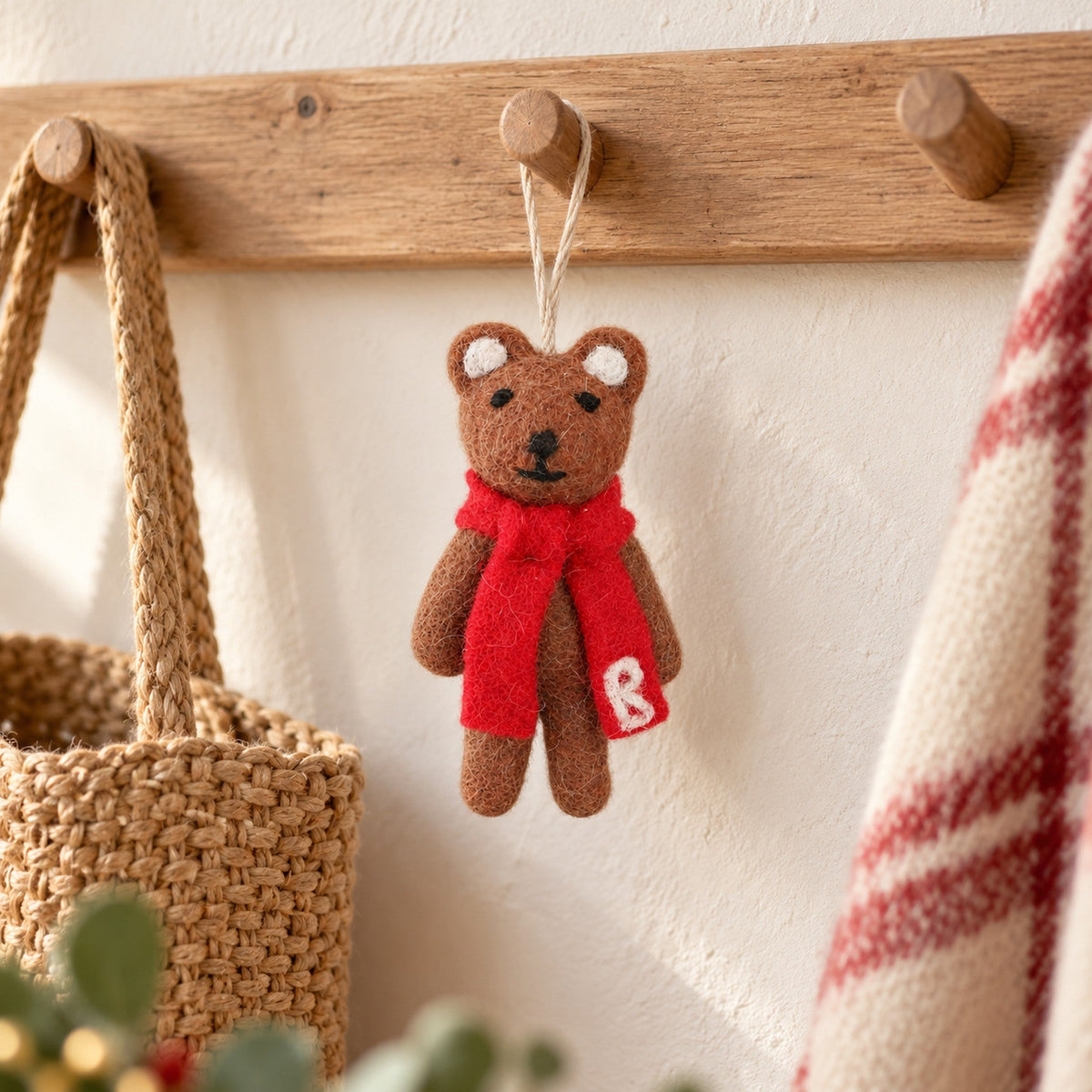 Bramble Bear, a slim brown felt bear with a long red scarf, hanging among Christmas tree branches.